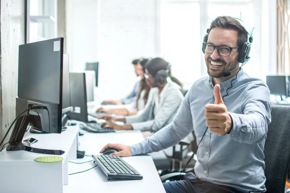 Lachender Mann im Call Center mit Headset zeigt Daumen hoch – Multichannel Services bei AP Dialog AG